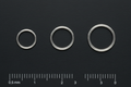 Three platinum full-ring marker bands in ascending width order on matte-black surface with reticle ruler