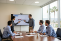 Four engineers around a conference table reviewing a catheter prototype, one annotating a cross-section drawing on a large monitor, M4D-branded materials, professional office setting