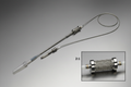Full stent delivery system on surgical-steel-gray background, diagonal orientation, 2:1 macro inset of stent-loaded balloon section with dual platinum full-ring marker bands at balloon shoulders