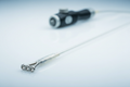 Steerable EP mapping catheter on white glass surface, 4-pole Pt/Ir electrode array in sharp foreground focus, bidirectional thumb-wheel handle soft-focused in background, cold diffused LED overhead lighting revealing translucent Pebax 35D distal shaft
