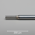 Nitinol coil-to-hypotube weld assembly on gray laboratory background with 200 µm scale bar